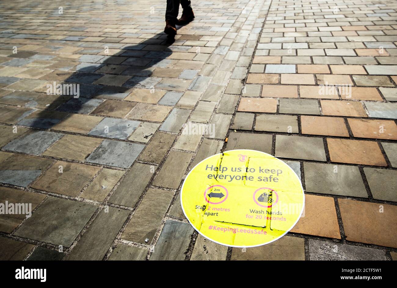 Das sich wandelnde Gesicht der Hauptstraße. Ein Mensch wirft einen Schatten, der an einem sozialen Distanzierungsschild im Stadtzentrum von Leeds vorbeigeht, das etwa sechs Monate nach dem Abend des 23. März, als Premierminister Boris Johnson landesweite Beschränkungen ankündigte, auf dem Bürgersteig gemalt ist. Stockfoto