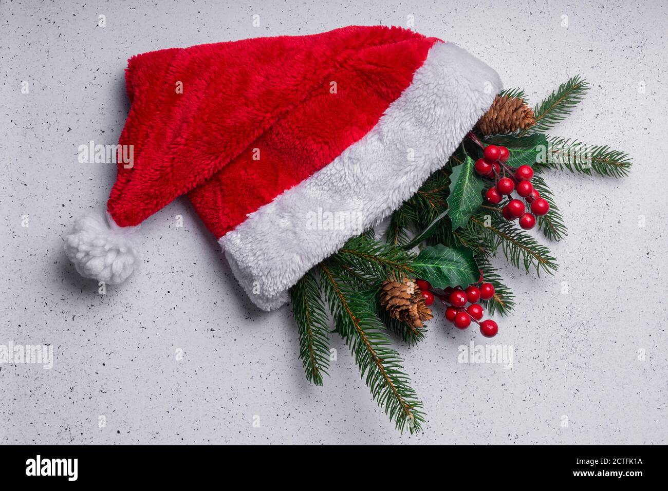 Selektiver Fokus. Weihnachtliche Lichtgestaltung, Baumzweige und Dekorationen in einem roten weichen Weihnachtshut Stockfoto