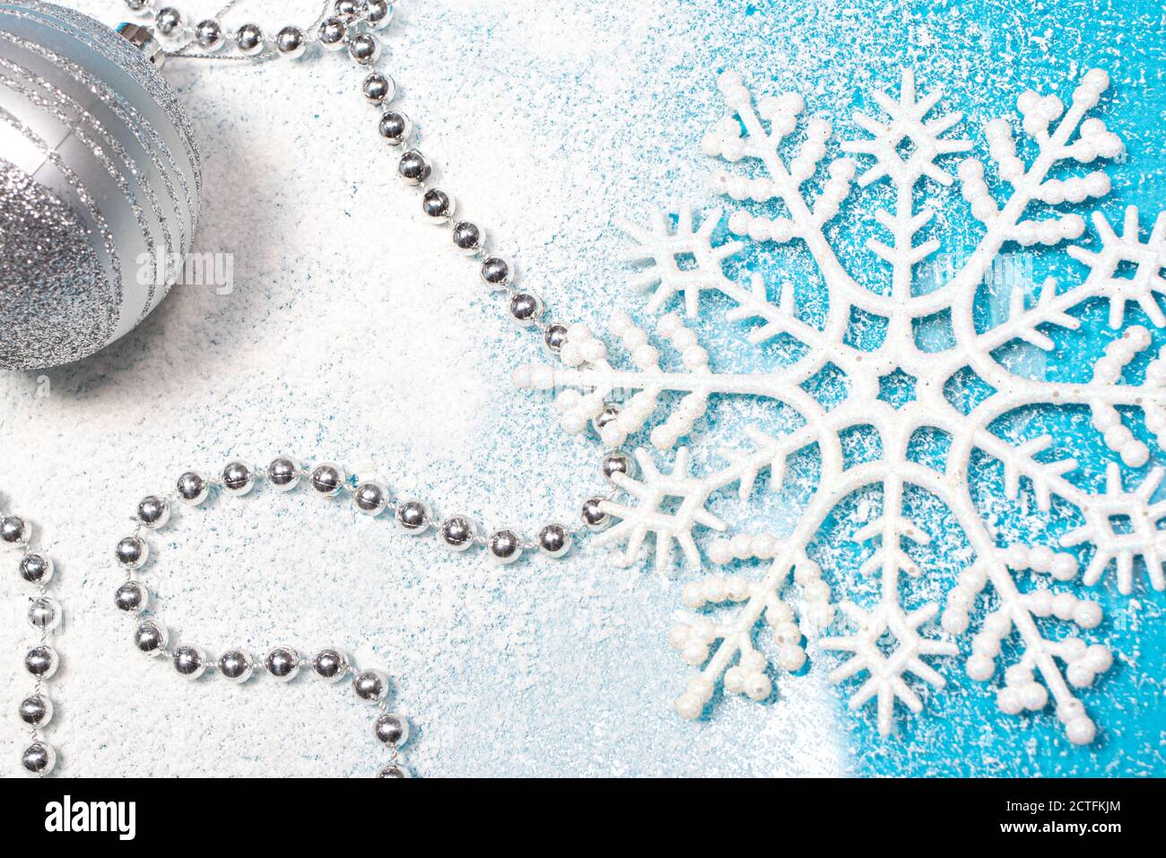 Schneeflocke, Perlen und ein Neujahrsspielzeug auf schneebedecktem blauem Hintergrund. Postkarte für Weihnachten, Winter festliches Dekor Stockfoto