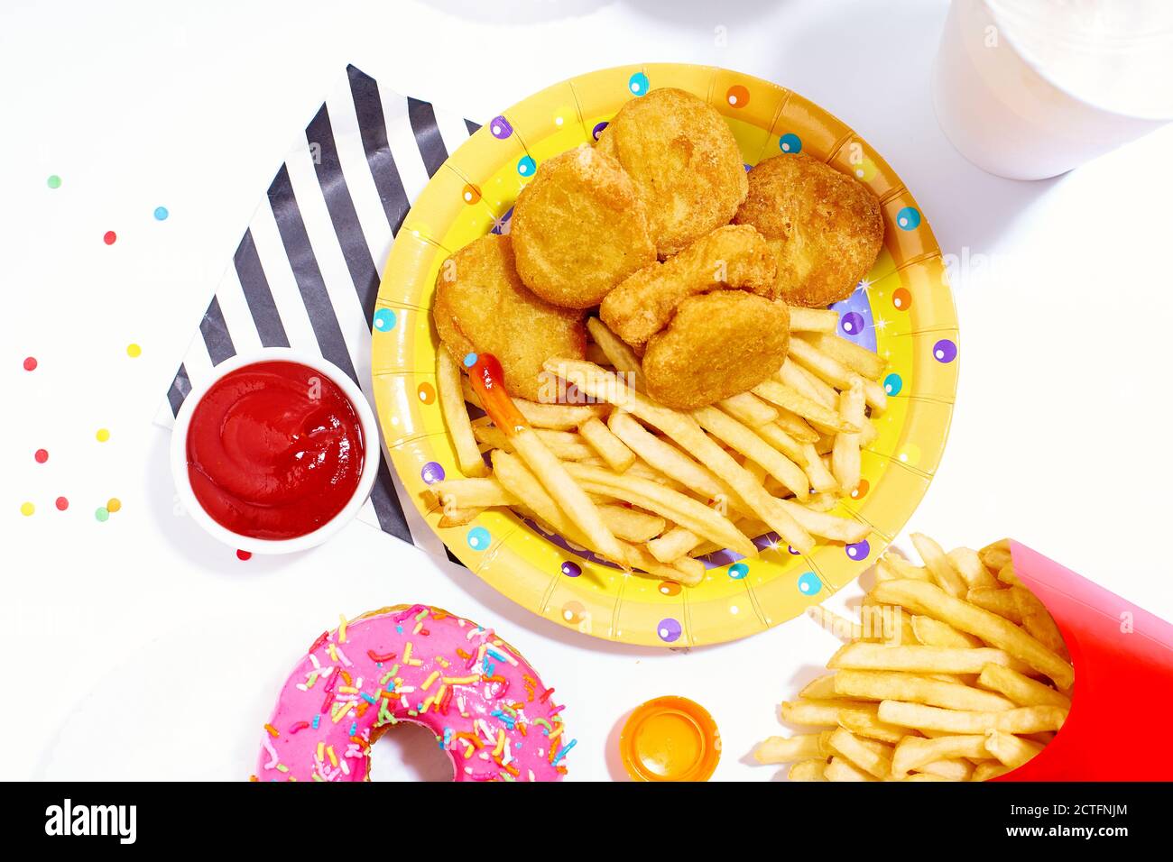 Junk-Food-Ansicht Mahlzeit von oben auf weißem Hintergrund. Pommes Frites, Chicken Nuggets, süß glasierte bunte Donuts mit Getränken und Sauce. Stockfoto