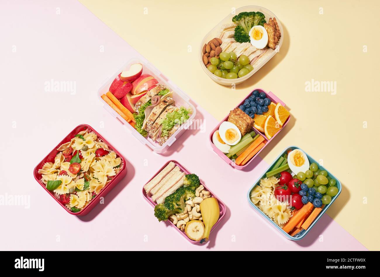 Draufsicht auf Schullunchboxen mit verschiedenen gesunden und nahrhaften Mahlzeiten Auf rosa Hintergrund Stockfoto