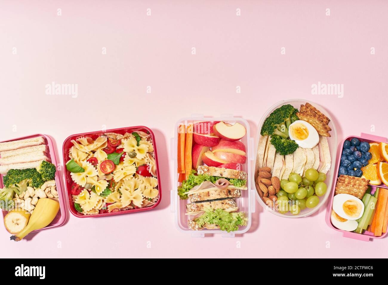 Draufsicht auf Schullunchboxen mit verschiedenen gesunden und nahrhaften Mahlzeiten Auf rosa Hintergrund mit Kopierbereich Stockfoto