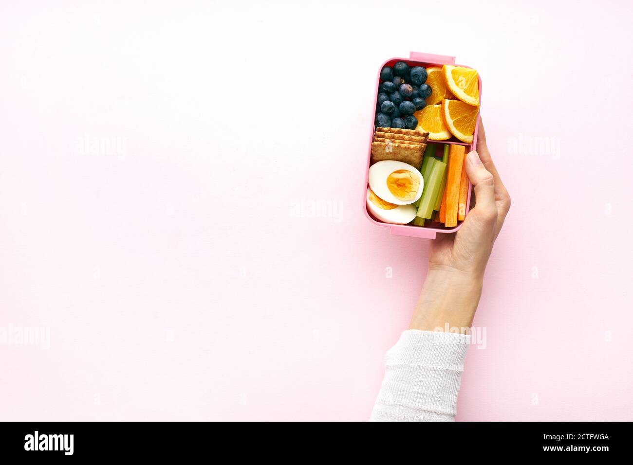 Weibliche Hände halten eine Lunchbox Draufsicht. Gesunde nahrhafte Mahlzeit mit Ei, Obst, Heidelbeere und Cracker in Behälter von oben mit Kopieplatz Stockfoto