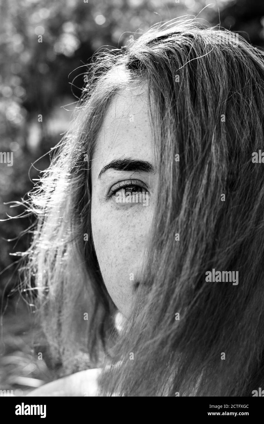 Nahaufnahme Porträt einer Frau Mädchen mit Sommersprossen. Porträt eines Mädchens im Freien im Sonnenlicht. Haare decken die Hälfte des Gesichts. Schwarz-Weiß-Porträt Stockfoto