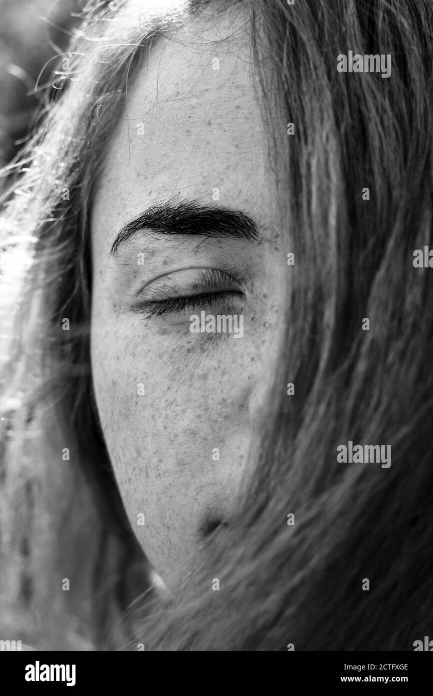 Nahaufnahme Porträt einer Frau Mädchen mit Sommersprossen. Porträt eines Mädchens im Freien im Sonnenlicht. Haare decken die Hälfte des Gesichts. Schwarz-Weiß-Porträt Stockfoto