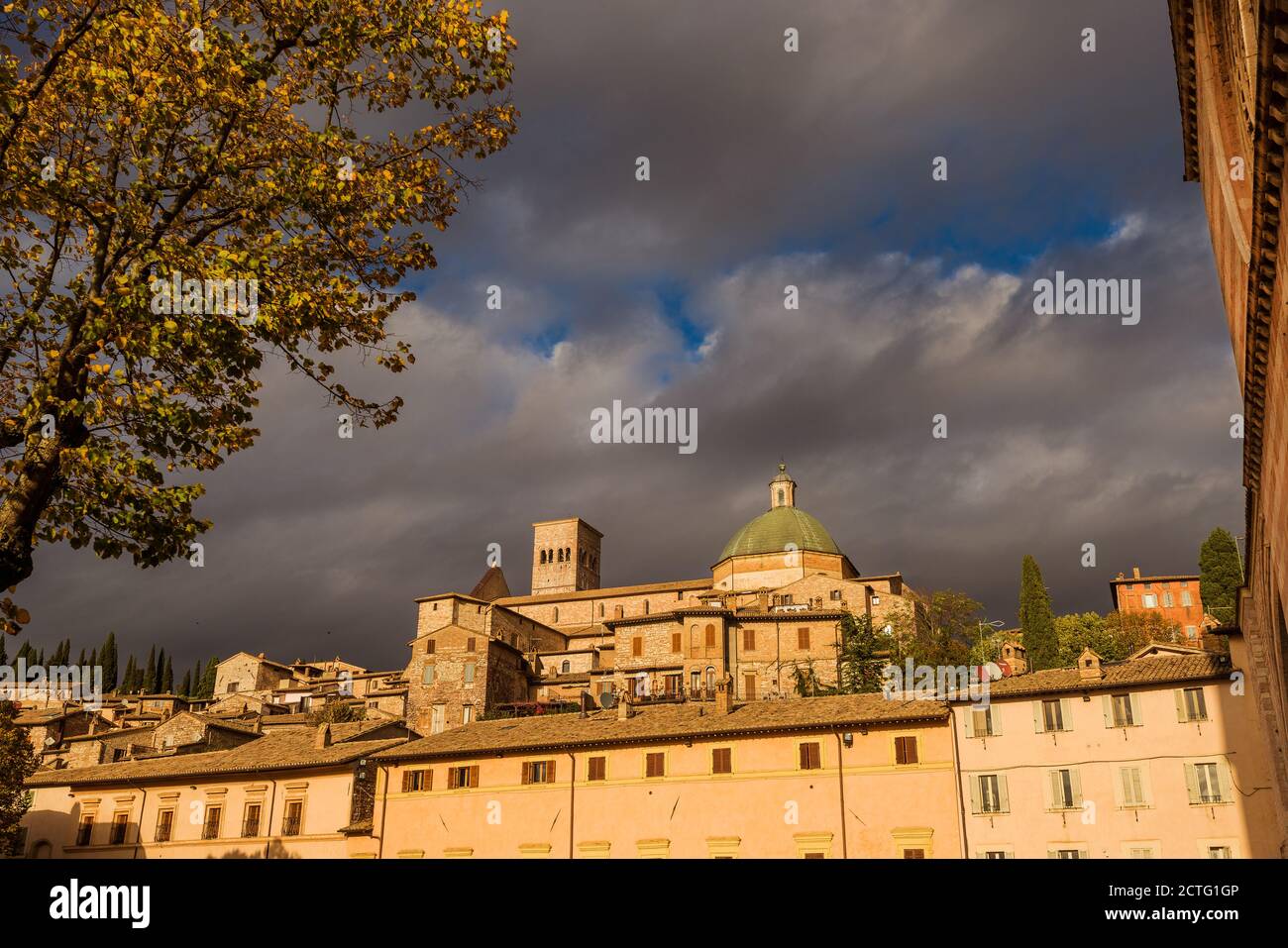 Herbst in Assisi. Blick auf die Kathedrale der Stadt und alte Gebäude von der St. Claire Kirche mit herbstlichen Blättern und goldenem Nachmittagslicht Stockfoto