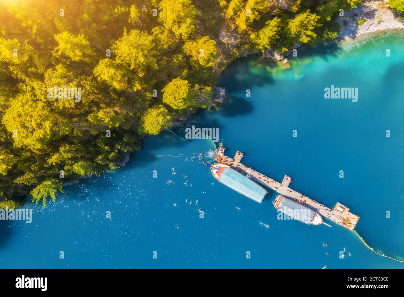 Luftaufnahme von Booten, hölzernen Steg in blauem See und grünen Bäumen Stockfoto