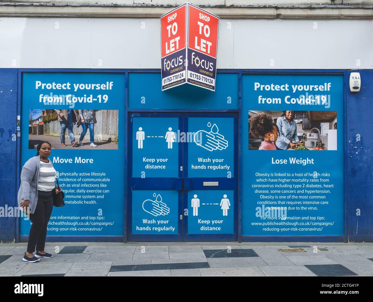 Eine Frau steht vor einem großen Plakat für die öffentliche Gesundheit in Slough und erinnert die Menschen daran, wie sie sich vor Covid schützen können. Stockfoto