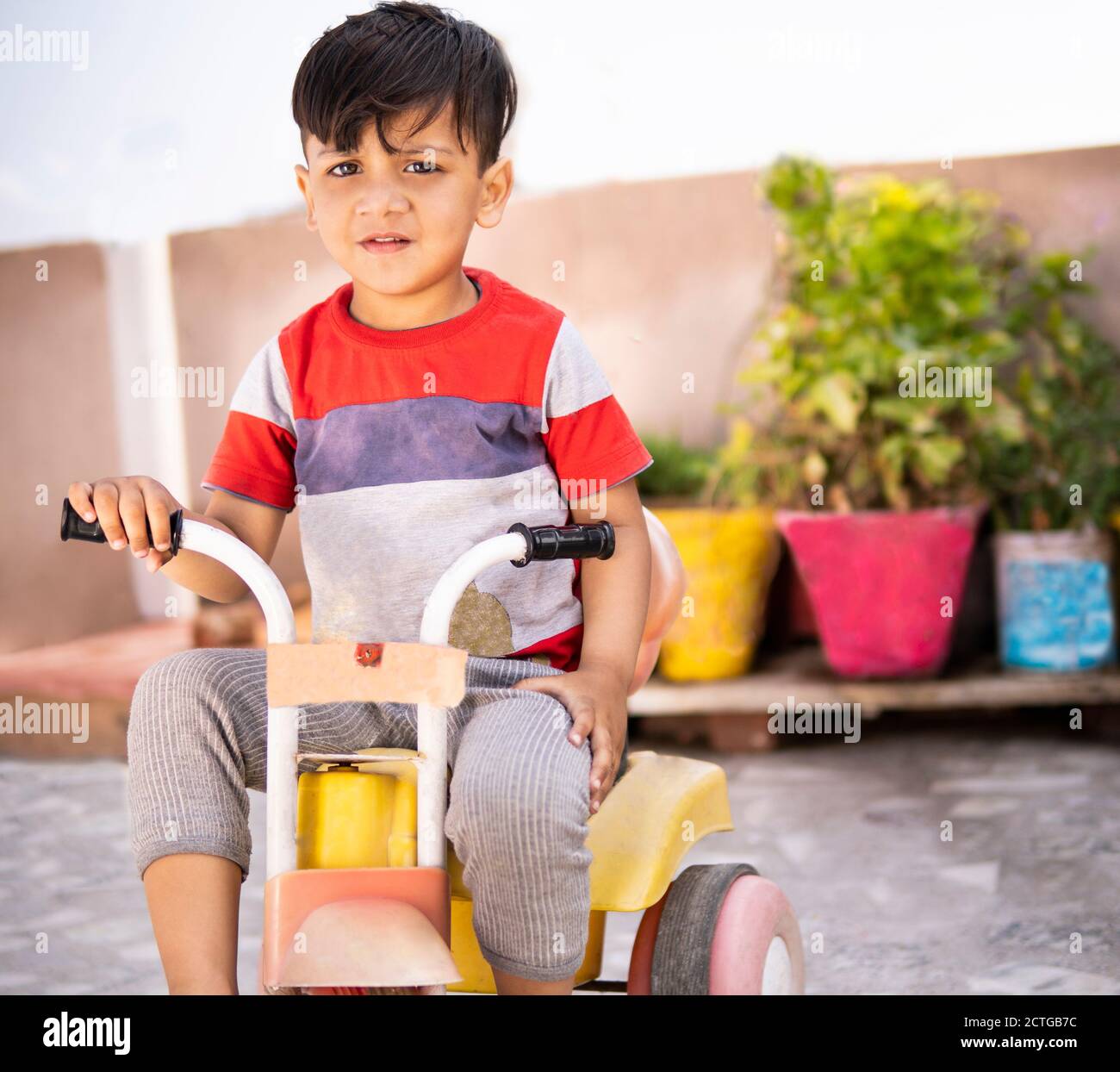 Netter kleiner Junge, der ein Dreirad für Kinder (Run Bike) auf dem Dach seines Hauses reitet und tagsüber Freizeit genießt. Stockfoto