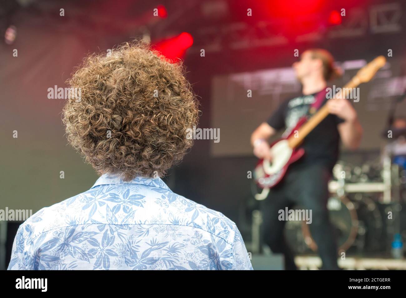 Junge Person mit sehr lockigen Haaren, die eine Rockband beobachtet Auf der Bühne Stockfoto