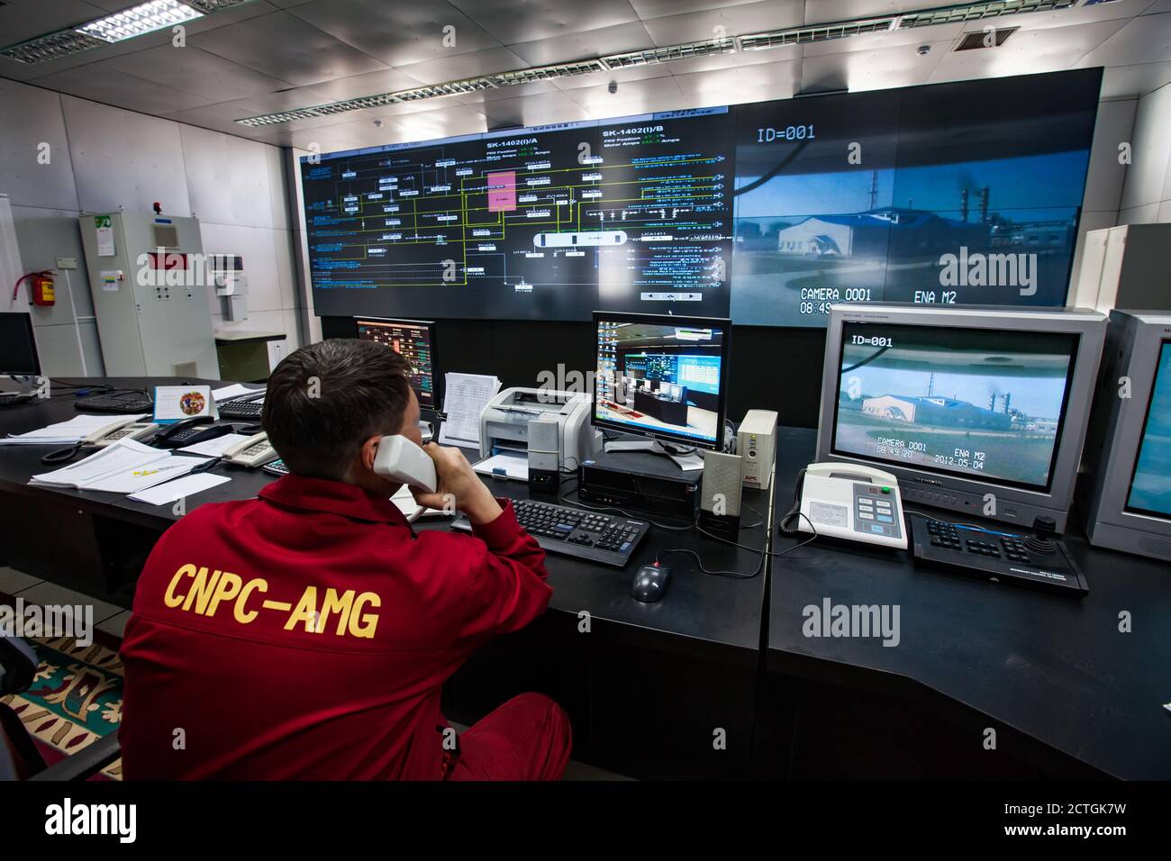 Ölraffinerie-Werk. Betriebsleitstelle und Bediener in rot Arbeitskleidung sieht auf Monitoren aus. CNPC-Unternehmen. Stockfoto