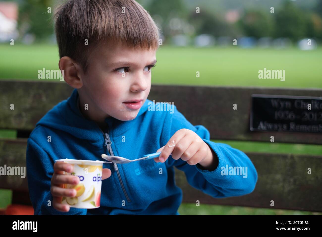 Vier Jahre alter Junge, der Joghurt auf einer Bank isst Ilkley West Yorkshire Stockfoto