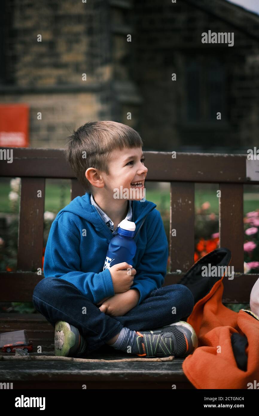 Der vierjährige Junge saß auf einer Bank mit Wasserflasche Lachend und glücklich Stockfoto