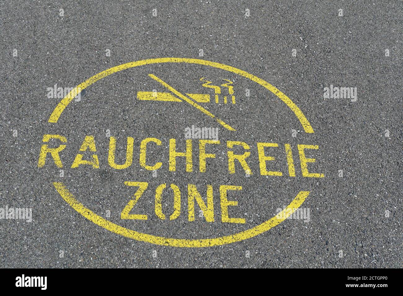 Ein rundes Schild für eine rauchfreie Zone auf der Straße oder Asphaltstraße in deutscher Sprache geschrieben mit einem Bild einer gestrichelten oder abgesagten Zigarette. Stockfoto