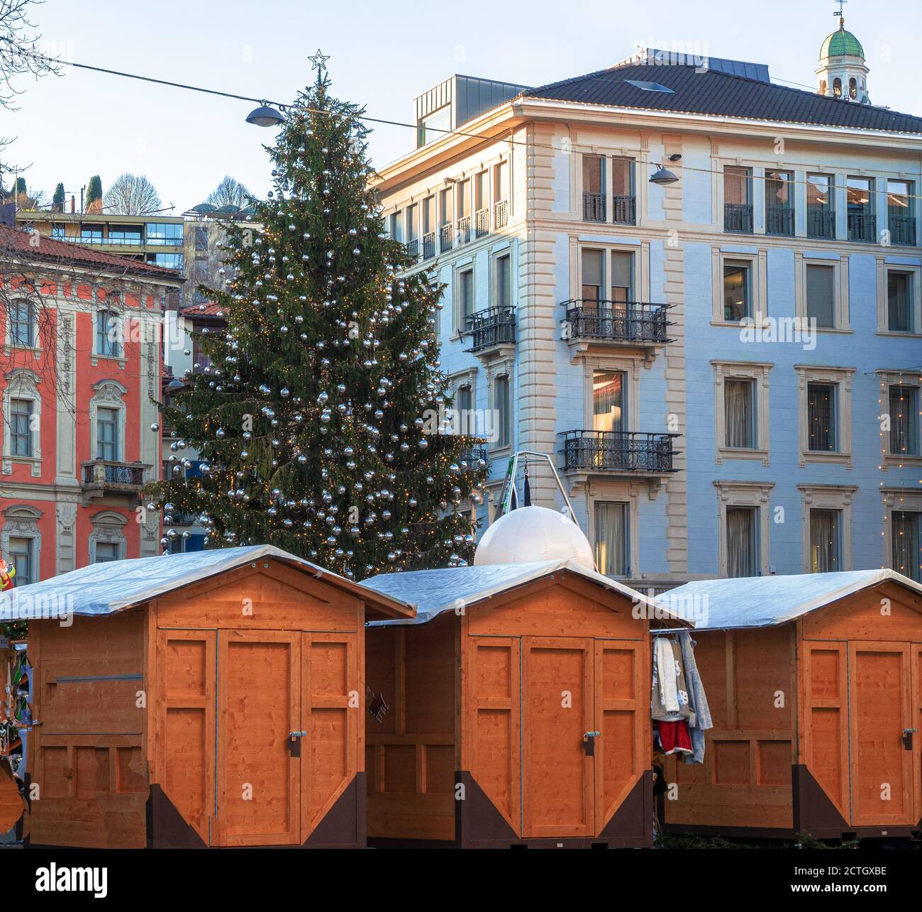 Platz mit einem großen Weihnachtsbaum und Holzhäusern für Märkte zwischen den eleganten Gebäuden von Lugano, Schweiz, dekoriert Stockfoto