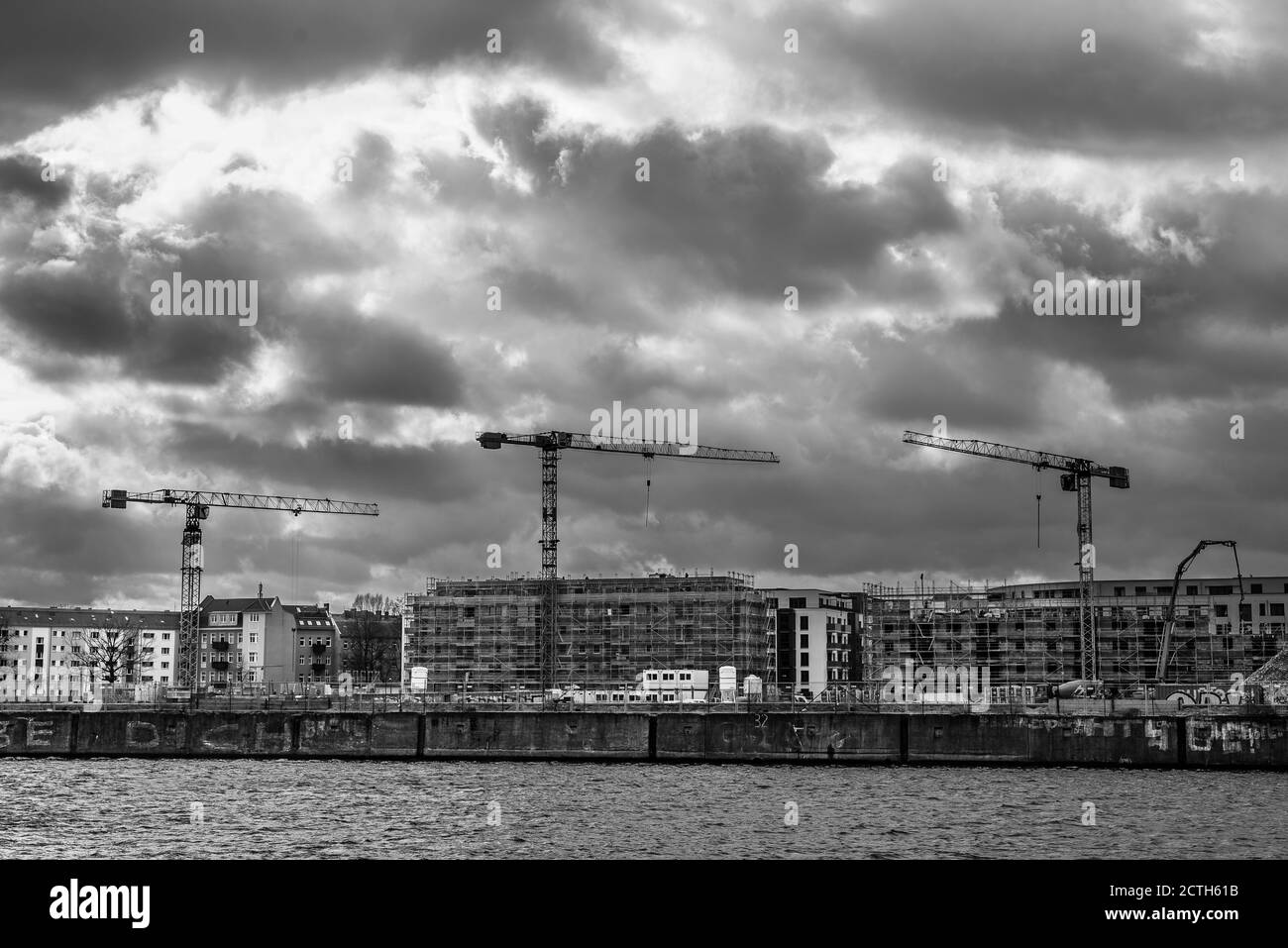 Eine Baustelle mit drei Kranen, Baustelle in Berlin, Deutschland, drei Krane auf einer Baustelle, dunkle Wolken, Schwarz-Weiß-Foto Stockfoto