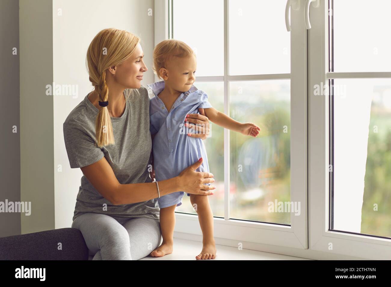Glückliche junge Mutter und kleines Kleinkind Junge beobachten Nachbarschaft aus Fensterbank Stockfoto
