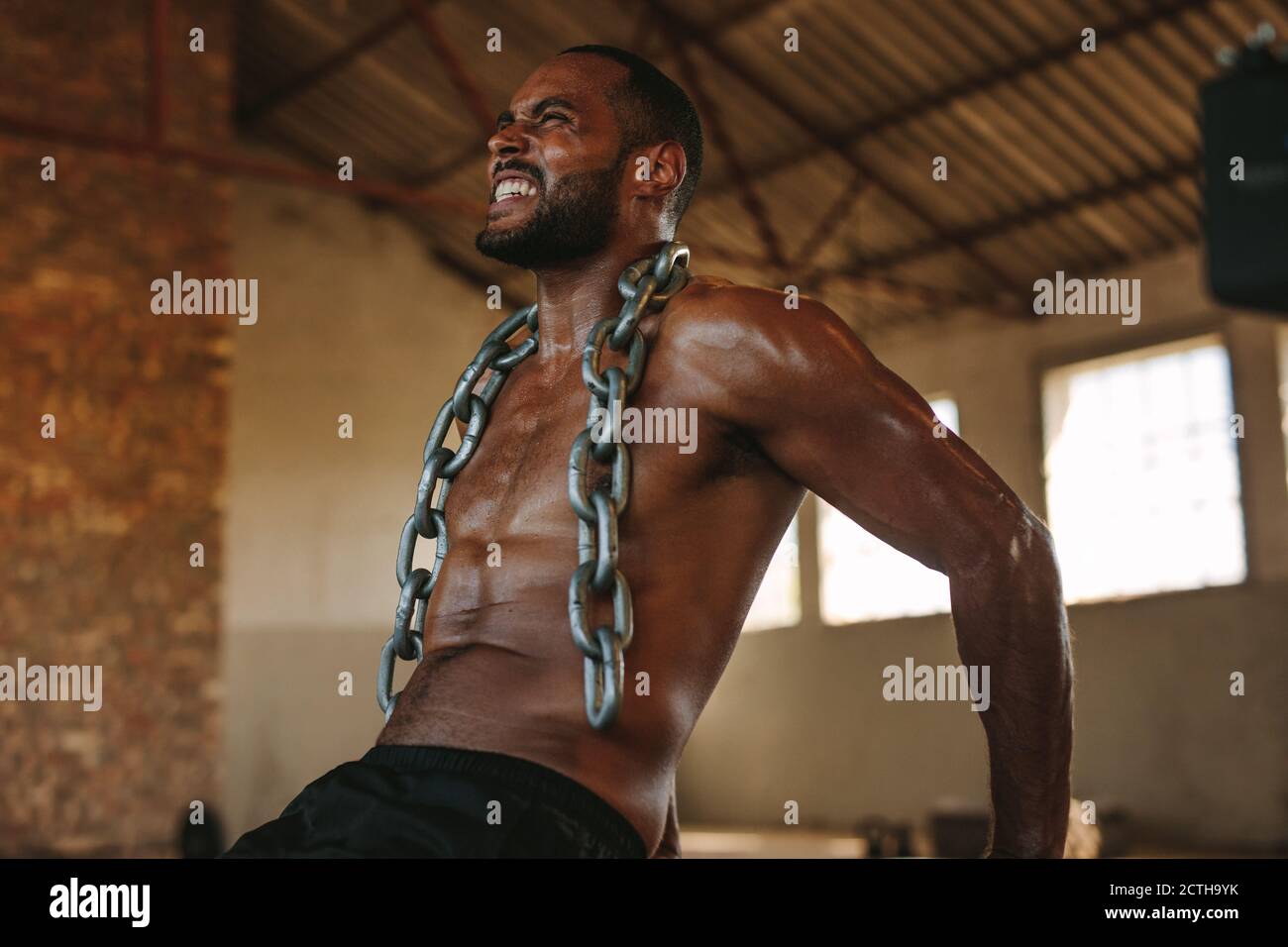 Ein harter Mann, der Trizeps-Dips-Übungen macht, mit einer Kette um den Hals. Fitness-Mann, der intensives Training im alten Lager macht. Stockfoto