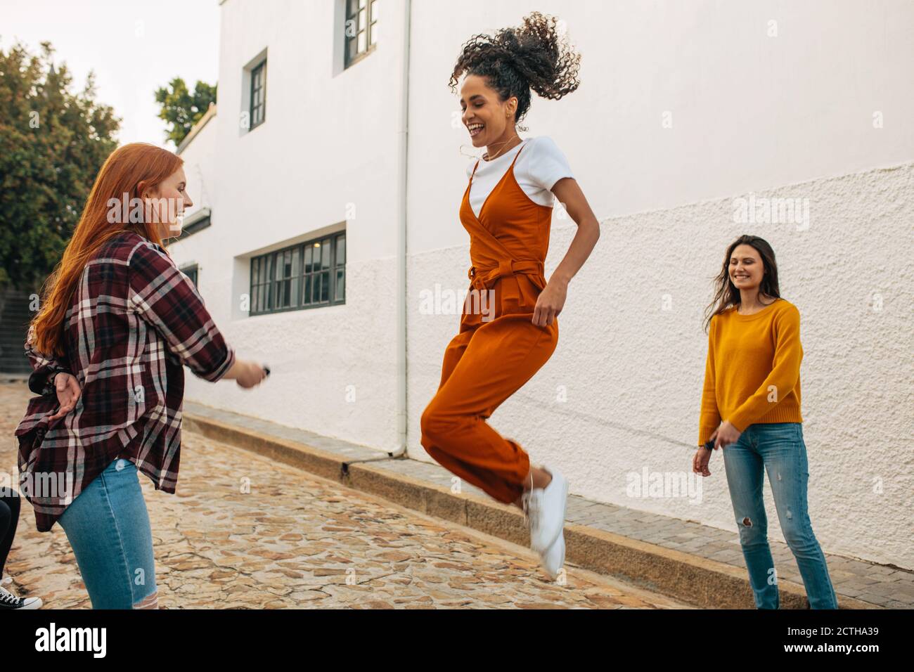 Zwei Frauen halten Springseil mit einem Freund springen. Gruppe von Freundinnen springen Seil zusammen. Stockfoto