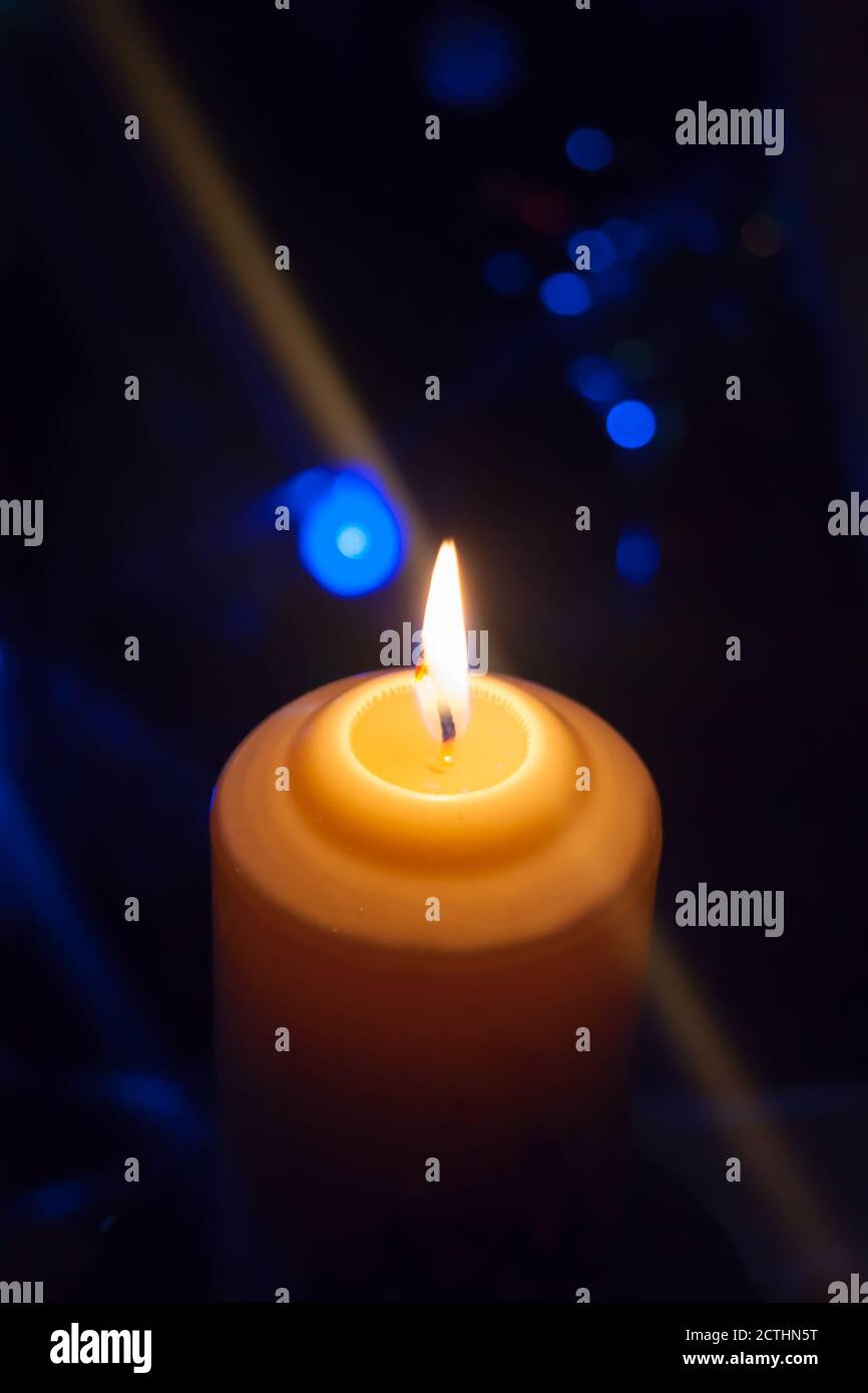 Eine große Kerze brennt vor dem Hintergrund einer Girlande mit strahlendem Licht. Vertikales Foto, Unschärfe. Mystische esoterische Romantik Divination Stimmung getauft Weihnachts-Karol-Setcer Stockfoto