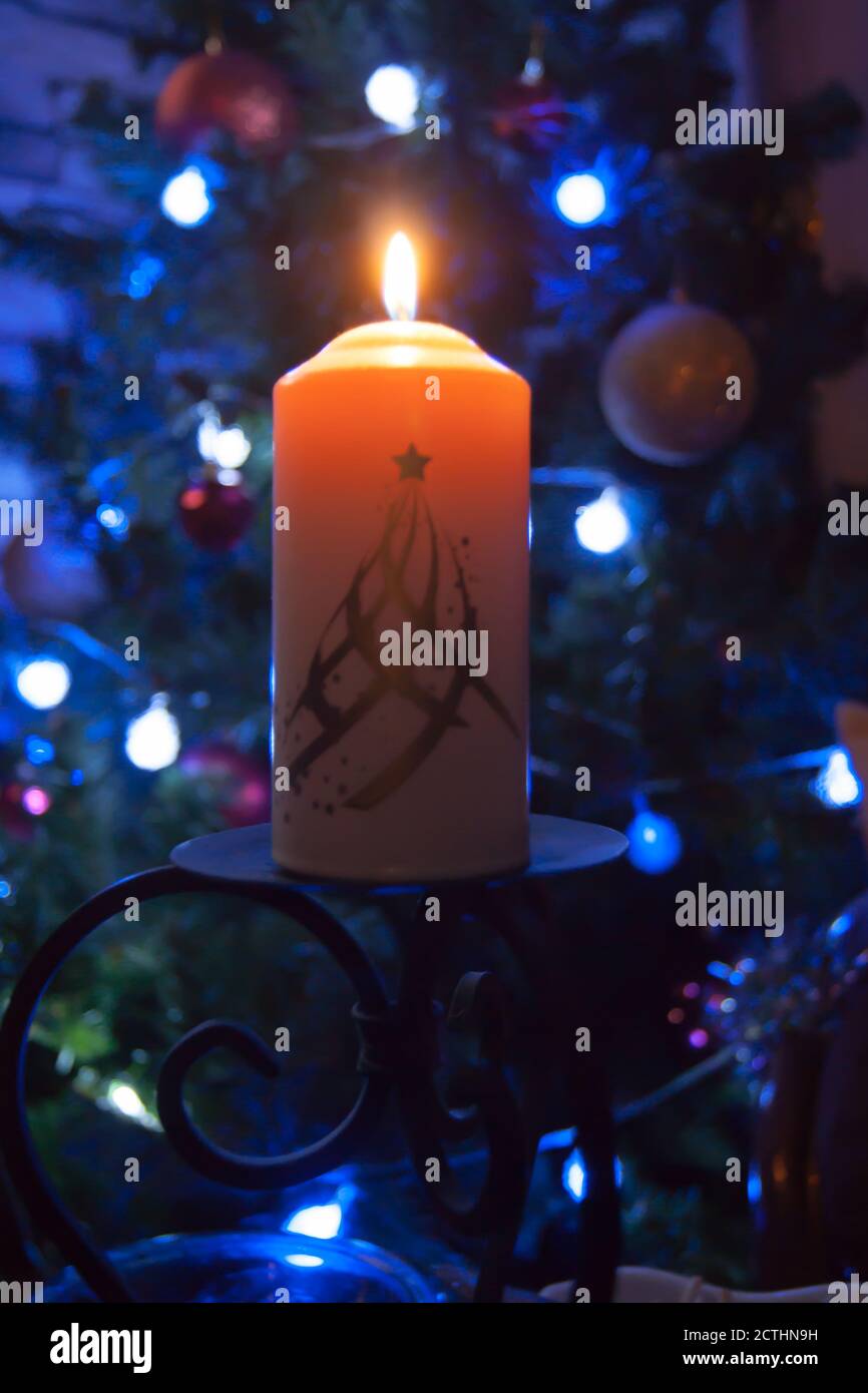 Eine große Kerze brennt vor dem Hintergrund einer Girlande mit strahlendem Licht. Vertikales Foto, Unschärfe. Mystische esoterische Romantik Divination Stimmung getauft Weihnachts-Karol-Setcer Stockfoto