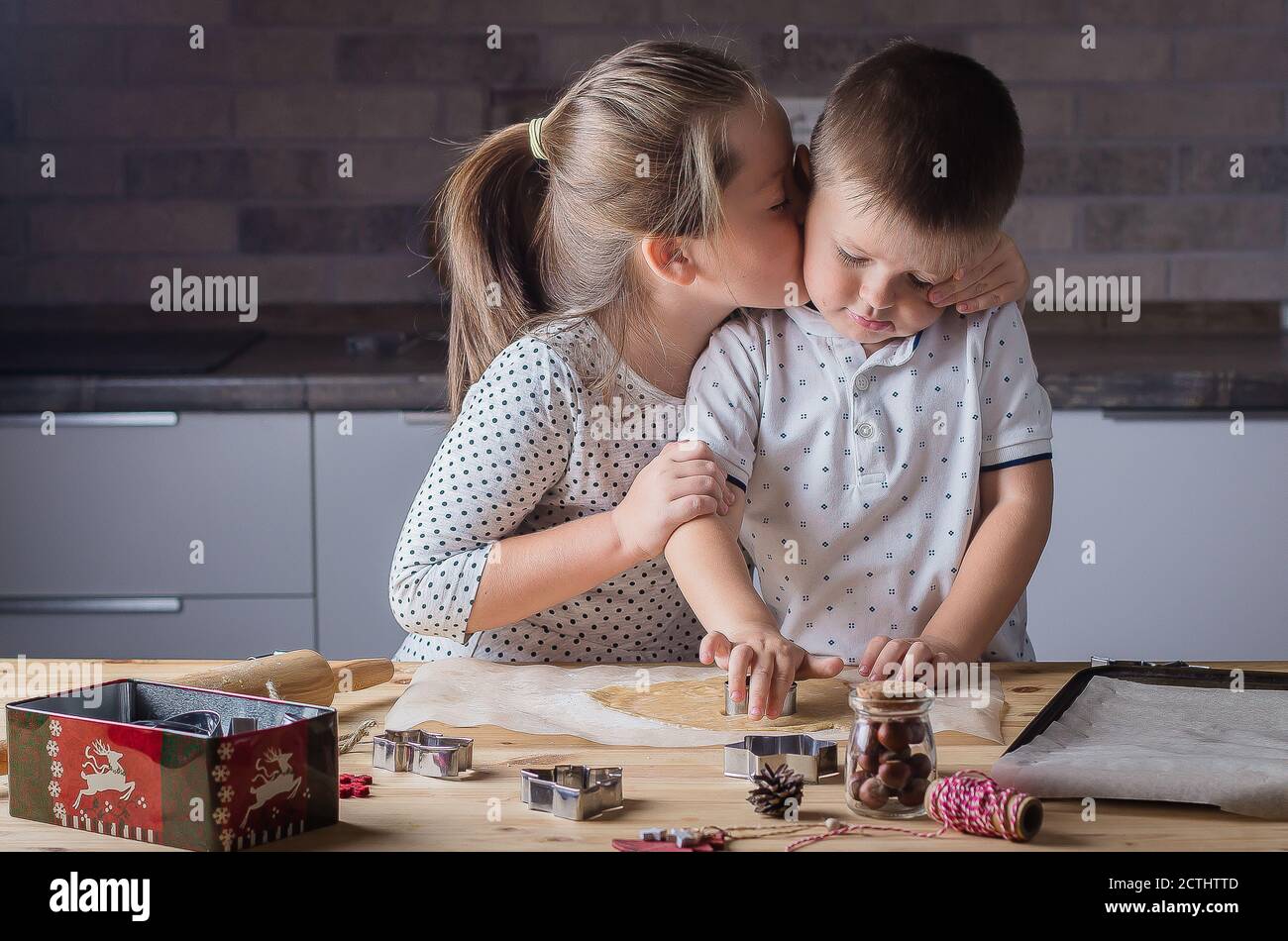 Holiday Sweet Food Konzept. Schwester küsst Bruder während der Herstellung weihnachtskekse. Roher Teig und Ausstecher für die Ferienkekse auf einem Holztisch. Stockfoto