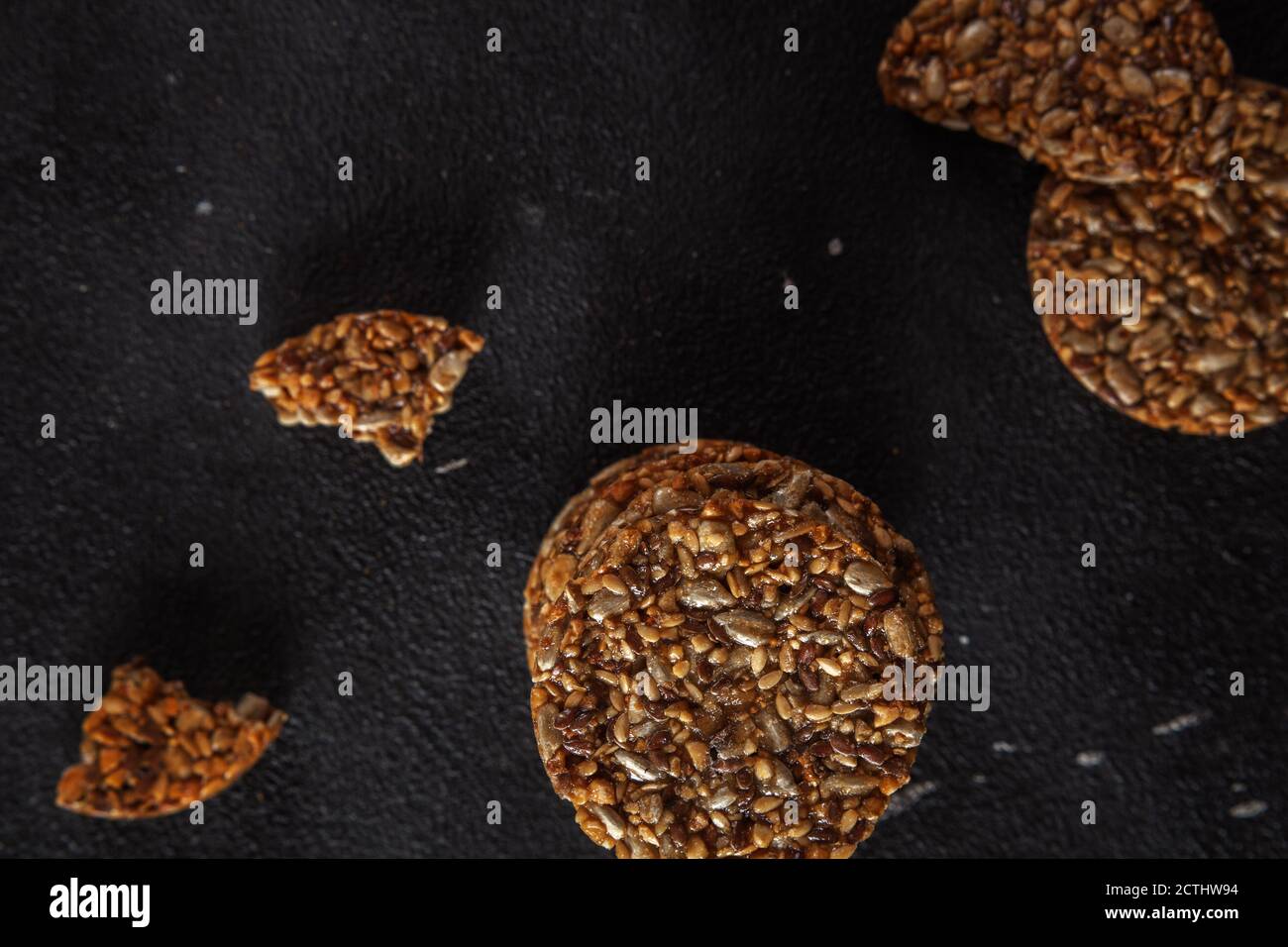 Karamell Erdnuss spröde aus Sonnenblumenkernen und Sesam und Fitness-Cookies mit Leinsamen auf dunkelschwarzem Beton Hintergrund. Stockfoto
