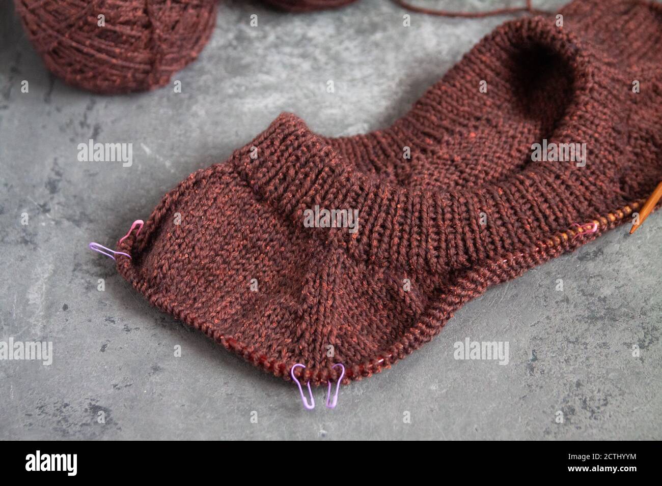 Brauner Pullover, Strickverfahren, Betonhintergrund. Raglannadeln. Woll-Webfäden. Stockfoto