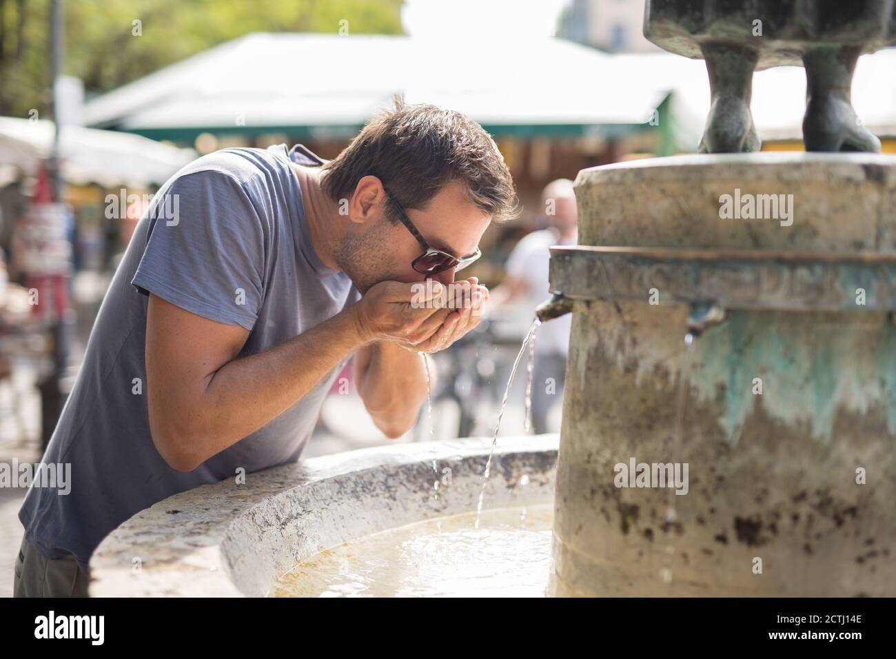 Durstige junge Casual cucasian Mann Trinkwasser aus der öffentlichen Stadt Brunnen an einem heißen Sommertag Stockfoto