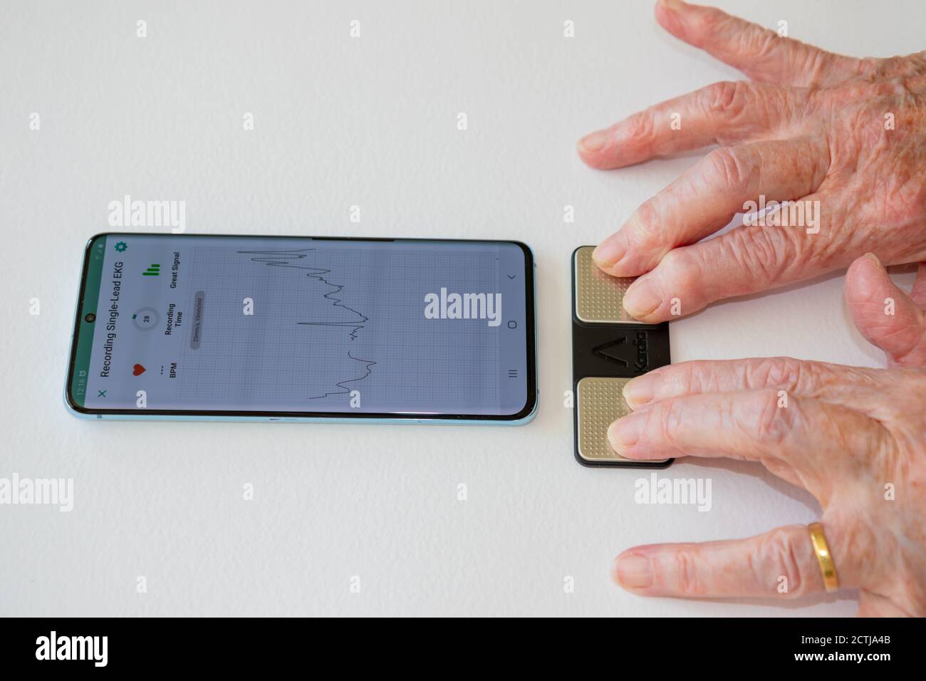 Person, die ein persönliches EKG-EKG-EKG mit der Kardiamobile AliveCor App auf dem Smartphone abnimmt. Finger auf gepaarten Elektroden platziert Stockfoto
