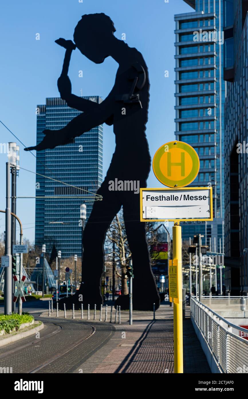 Frankfurt, Hessen, Deutschland: Schild der Straßenbahnhaltestelle Festhalle/Messe vor der monumentalen kinetischen Skulptur "Hammering man" von Jonathan Borofsky. Stockfoto