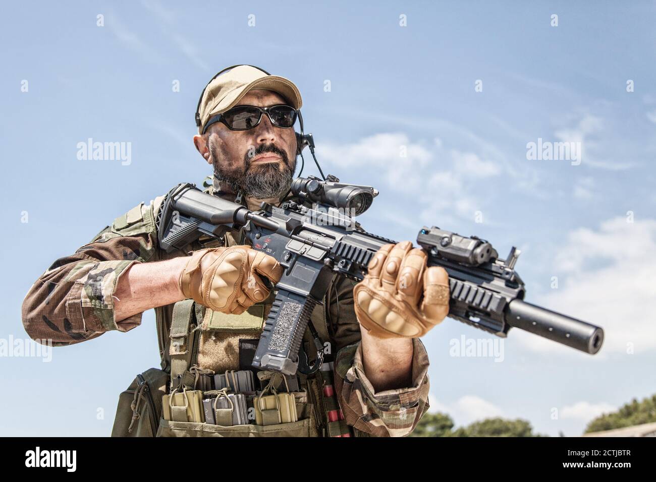 Private militärische Firma Söldner, brutal aussehende Spezialeinheiten Kämpfer in der Schlacht Uniform und Plattenträger, trägt Radio-Headset und Sonnenbrille, hält Service Gewehr in den Händen, bereit zu kämpfen Stockfoto