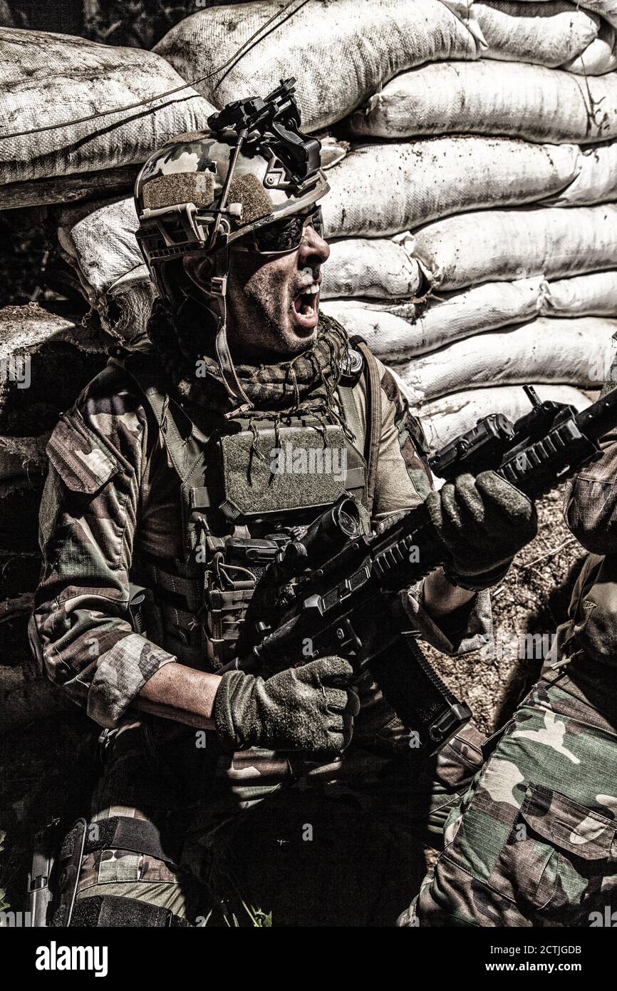 Navy versiegelt Schütze, Soldat in Kampfuniform und Helm, greifen Sturmgewehr, schreien, schreien, während hinter Sandsäcken zu decken. Special Forces Infantryman Angriff Feinde in Graben Stockfoto