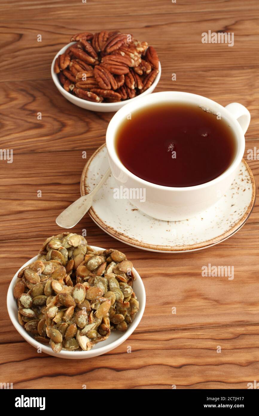 Mit Zucker beschichtete Kürbiskerne Kekse, Pekannüsse in einer Schüssel und eine Tasse schwarzen Tee auf einem Holztisch. Nahaufnahme Stockfoto