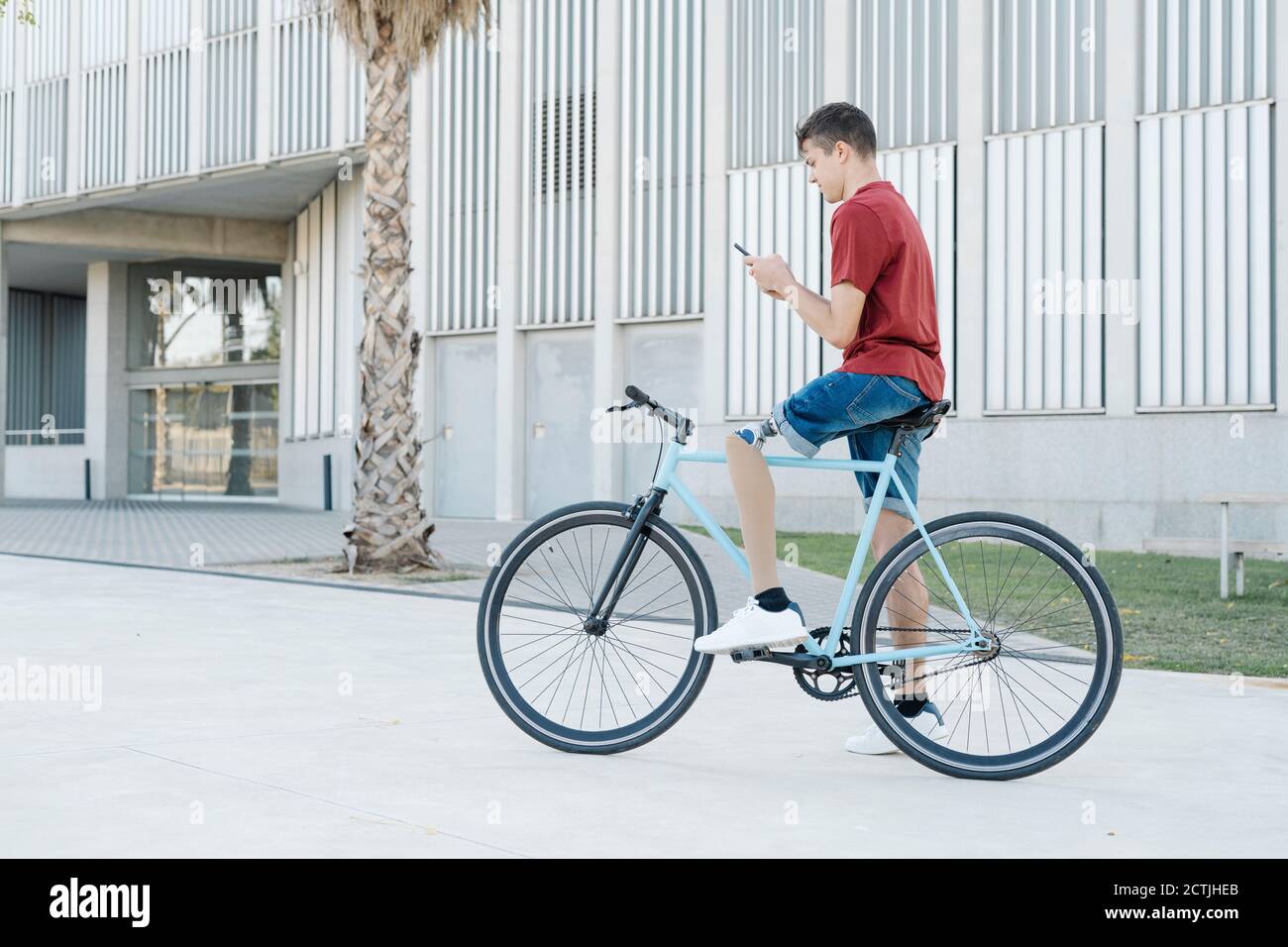 Junger Mann mit Beinprothese sitzt auf dem Fahrrad und Messaging Auf dem Smartphone in der Stadt Stockfoto