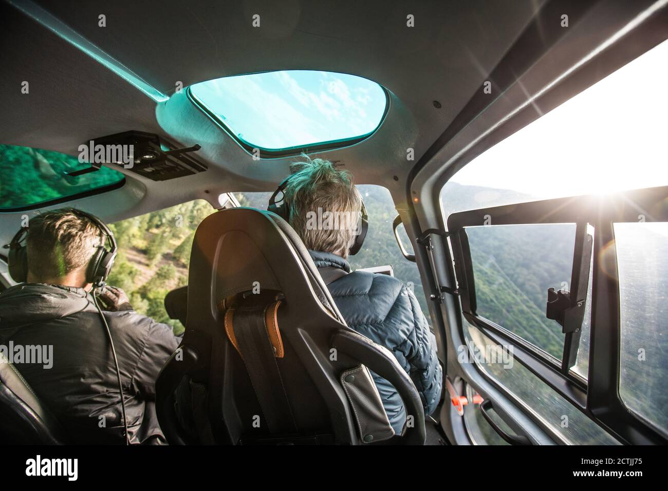 Rückansicht des Hubschrauberpiloten, der tief durch bewaldete Berge fliegt. Stockfoto