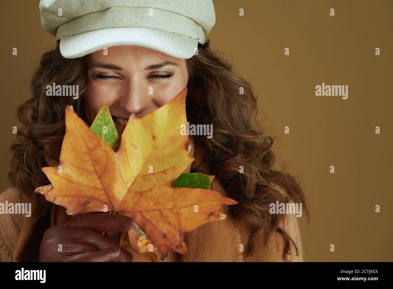 Hallo Herbst. Happy trendy 40 Jahre alte Hausfrau in Pullover mit Lederhandschuhen und gelben Herbst Ahornblätter auf Bronze Hintergrund. Stockfoto
