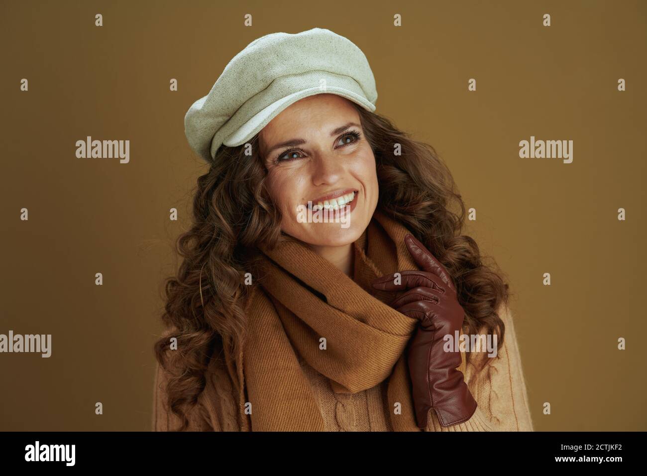 Hallo september. Nachdenkliche junge Frau im Schal mit Lederhandschuhen isoliert auf beigem Hintergrund. Stockfoto