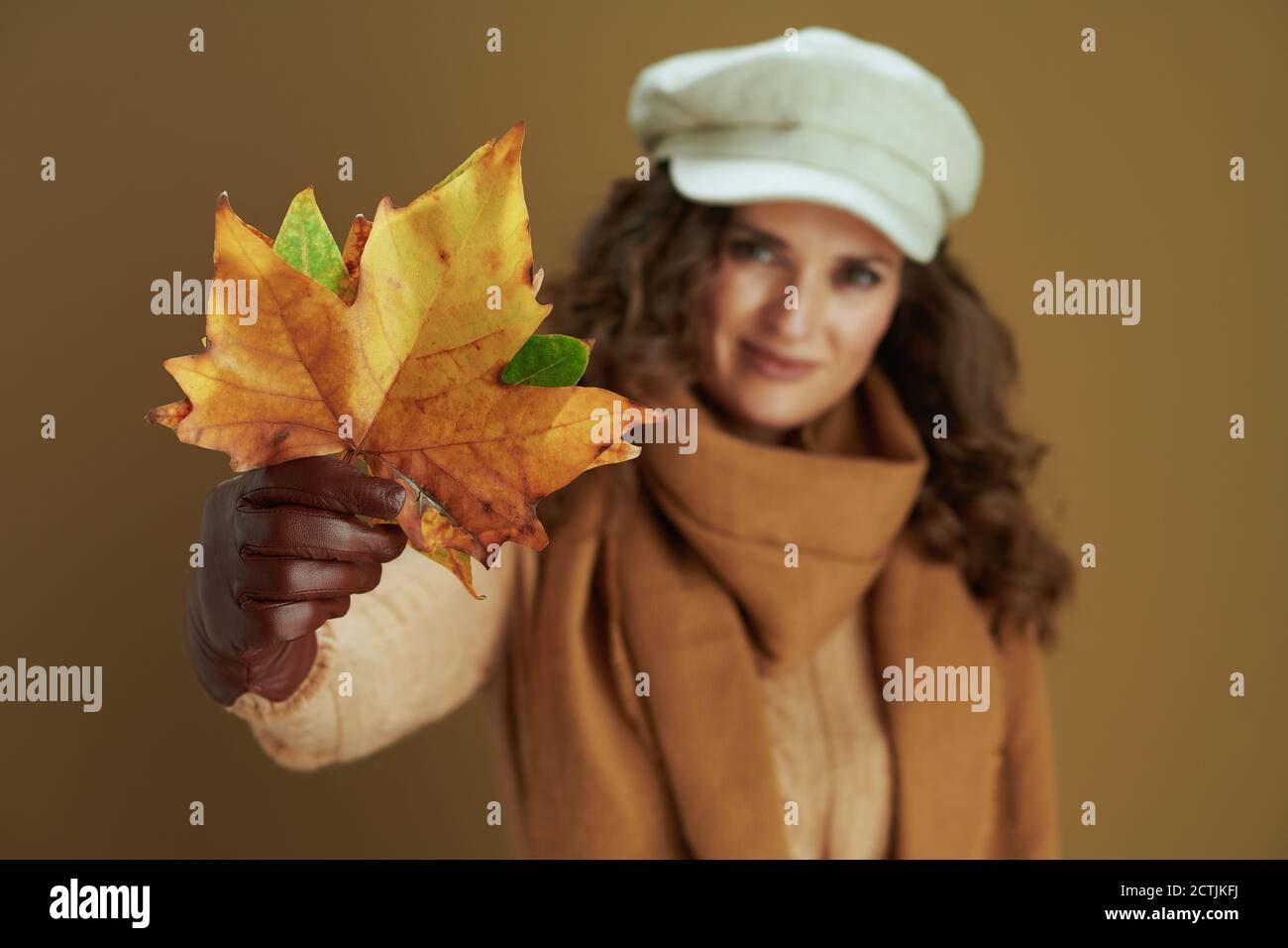 Hallo Herbst. Glücklich elegante Frau mittleren Alters im Schal mit Lederhandschuhen und gelben Herbst Ahornblätter auf braunem Hintergrund. Stockfoto