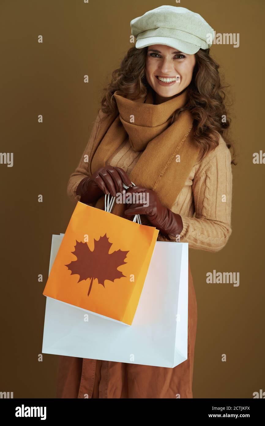 Hallo september. Lächelnd moderne Frau in Schal mit Lederhandschuhen und Papier Einkaufstasche isoliert auf Bronze Hintergrund. Stockfoto
