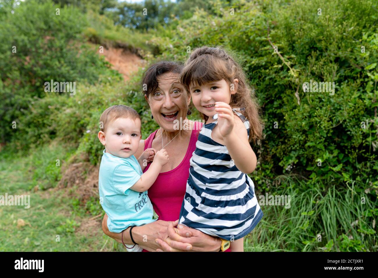 Fröhliche Großmutter trägt Enkelinnen im Feld Stockfoto