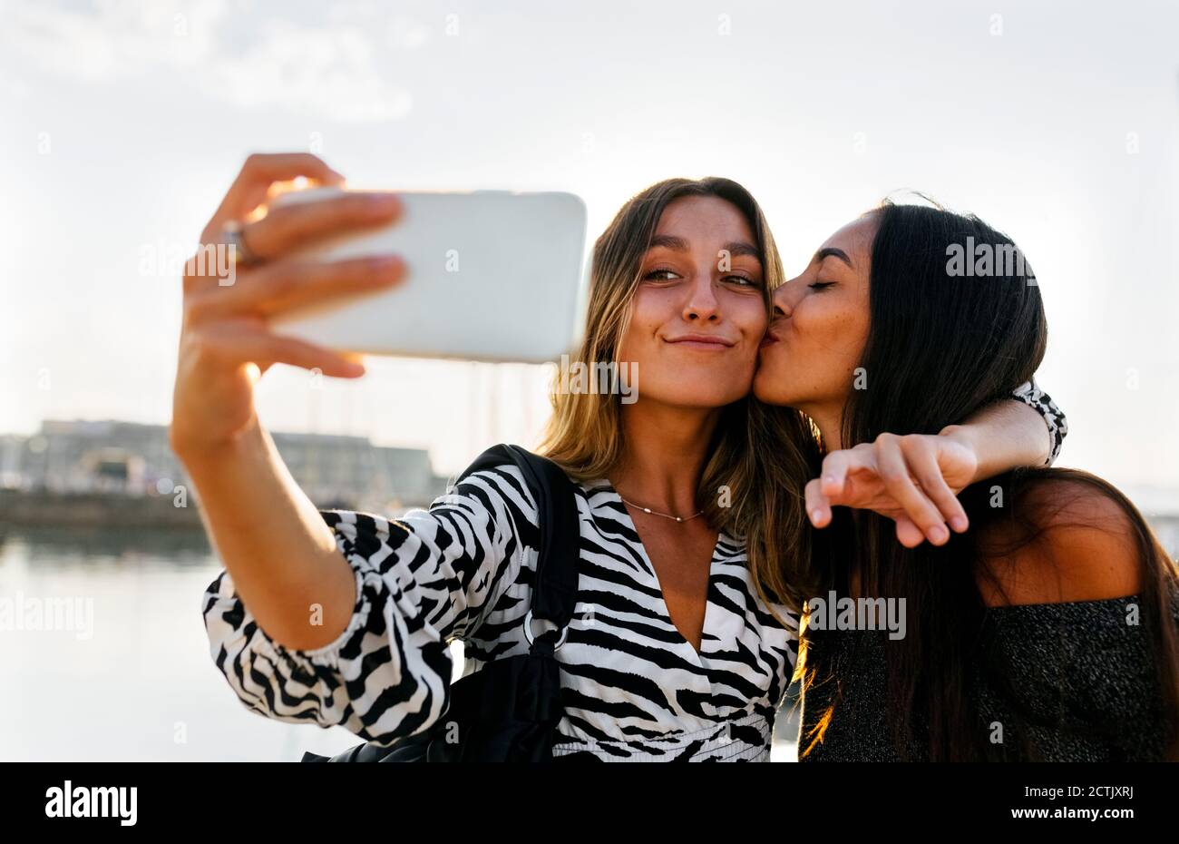 Junge Frau küsst Freund während Selfie gegen klaren Himmel Stockfoto