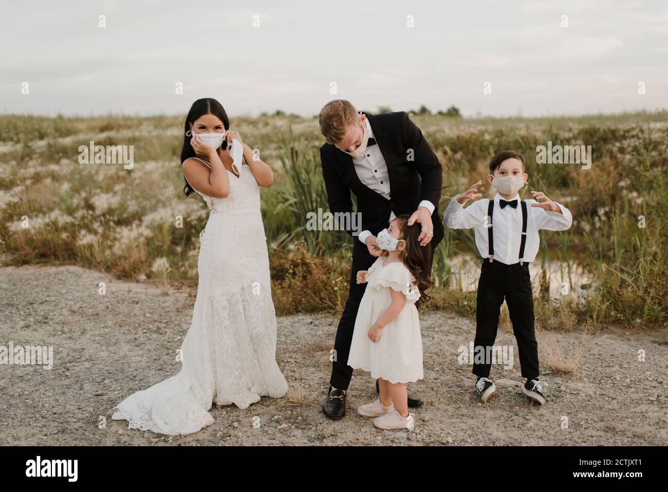 Eltern mit Kindern im Hochzeitskleid tragen Gesichtsmaske, während Während des COVID-19 im Feld stehen Stockfoto
