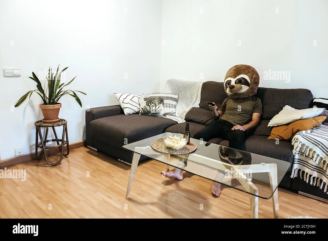 Mann trägt Teddybärmaske und schaut beim Entspannen fern Sofa im Wohnzimmer Stockfoto