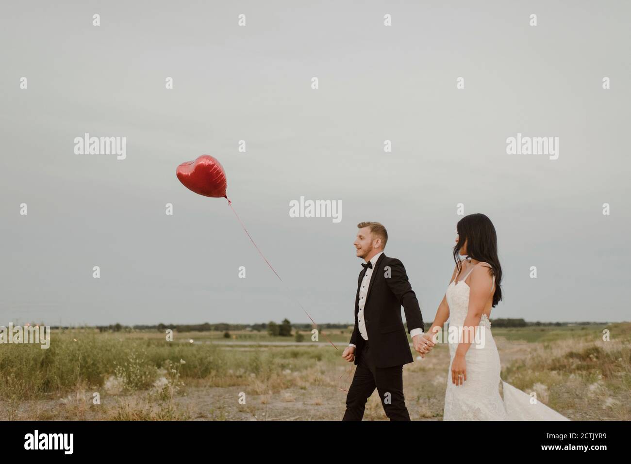 Braut und Bräutigam mit Herz-Form Ballon hält die Hände während Gegen den klaren Himmel laufen Stockfoto