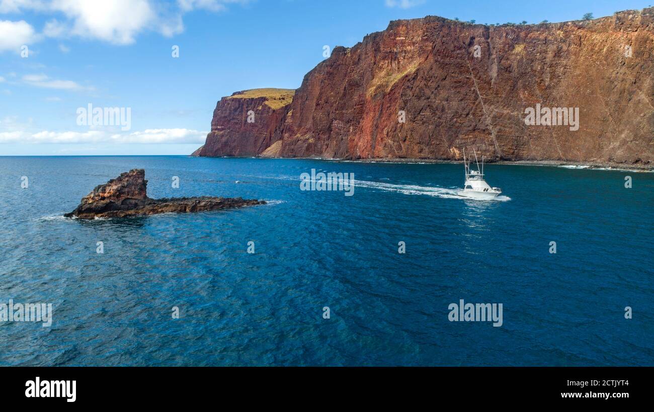 Eine Luftaufnahme eines Charterfischereibootes, das entlang der Klippen und Sharkfin Rock auf der Südwestseite der Insel Lanai, Hawaii, USA, fährt. Stockfoto