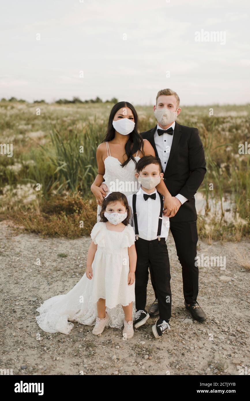Eltern und Kinder im Hochzeitskleid tragen eine schützende Gesichtsmaske Während des COVID-19 im Feld stehend Stockfoto