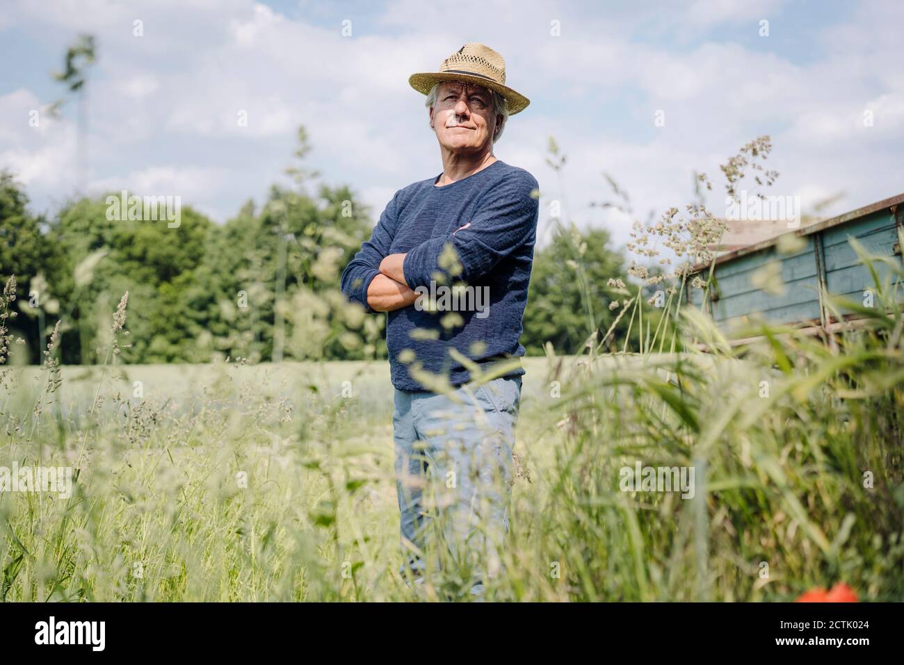 Lächelnder Mann mit Hut und gekreuzten Armen im Hof Stockfoto