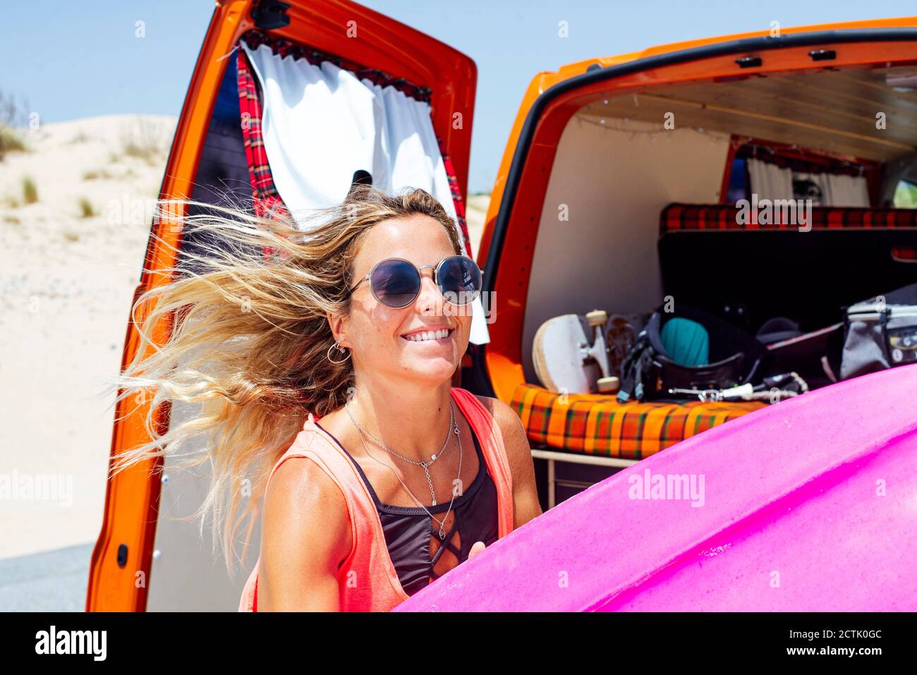 Wind weht Haare von jungen Frau halten Surfbrett während stehen Gegen den Kofferraum Stockfoto