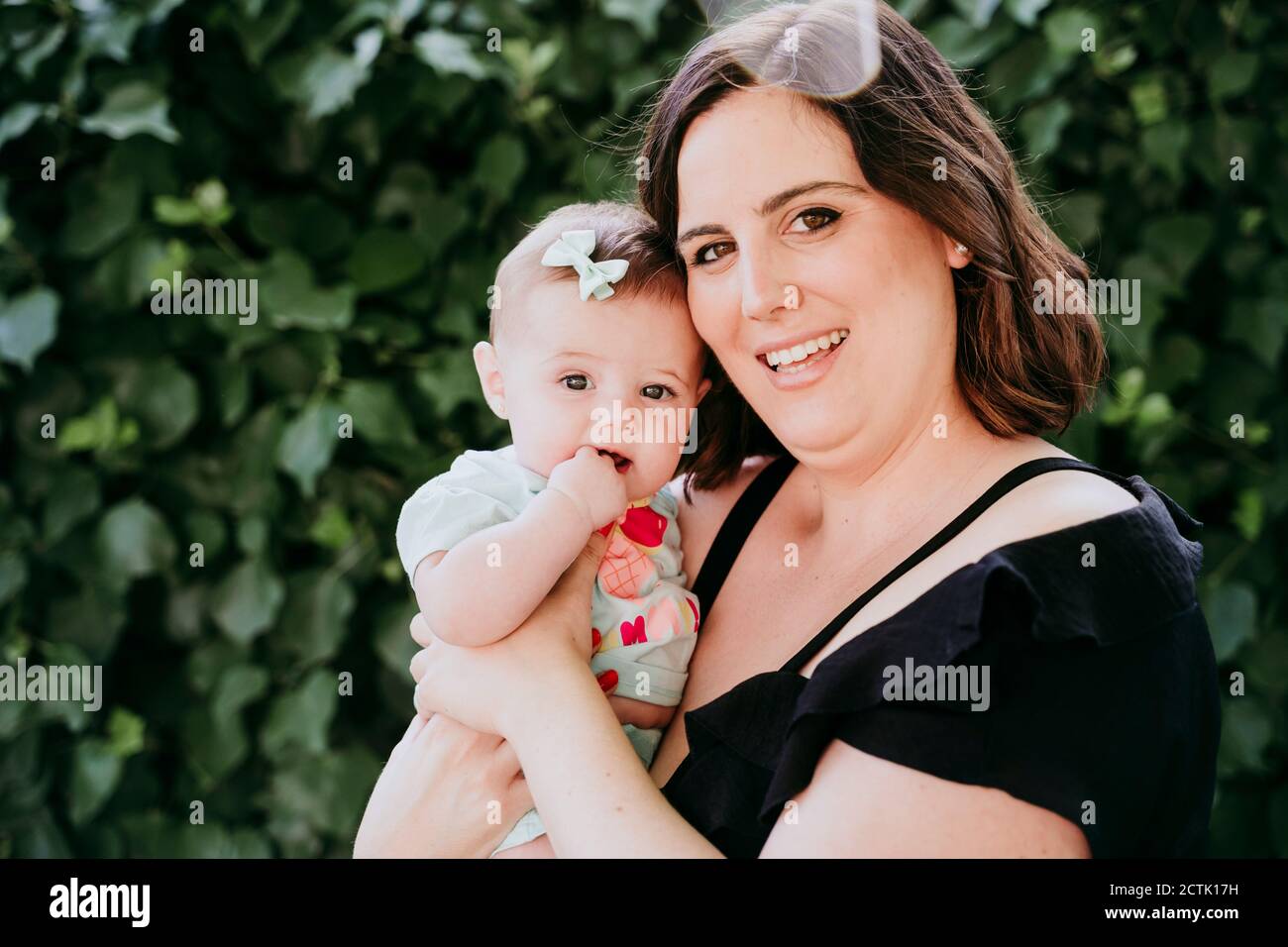 Lächelnde Mutter hält Baby Mädchen gegen Efeu Stockfoto